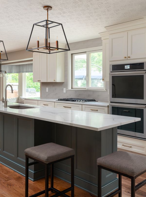 Welcoming kitchen with warm white cabinets, blue island, marble quartz counters, stainless steel.