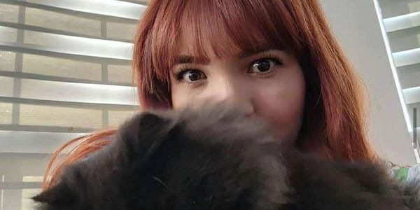 A woman with red hair peeks over a fluffy black cat.