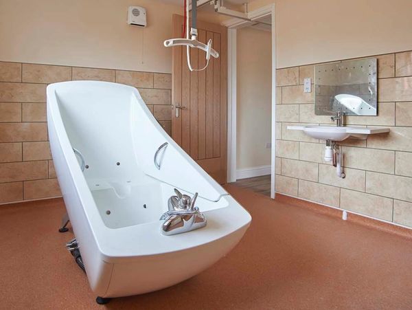 Accessible bathroom set up featuring adjustable bath and ceiling hoist.