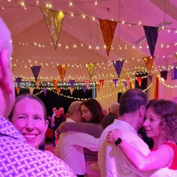 Couples dancing under colorful bunting and string lights at a lively indoor party.