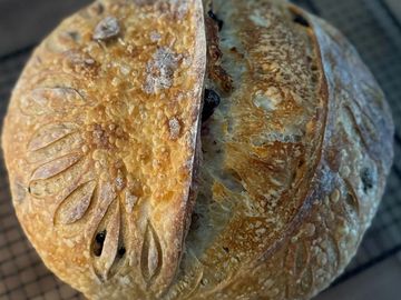 A round loaf of artisan bread with decorative scoring and a golden crust.