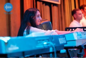 Woman playing keyboard on stage with focused expression.