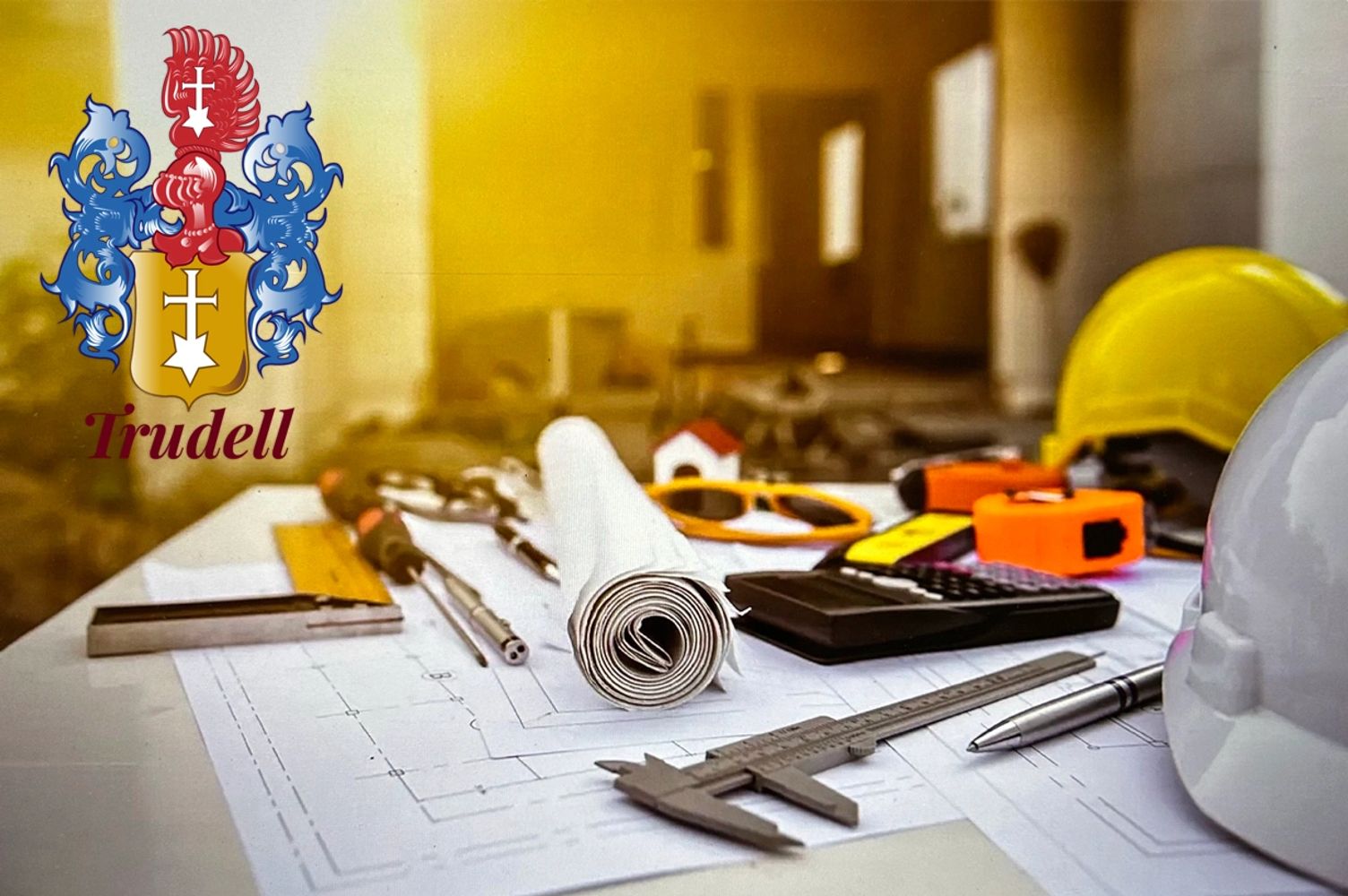 Architectural tools and blueprint on a desk with Trudell logo.