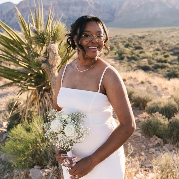 Smiling bride in a white dress holding a bouquet in a desert landscape.