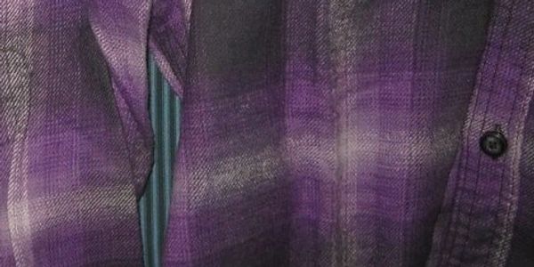 A close-up of the arm and chest of a rumpled purple and black flannel plaid nightshirt.
