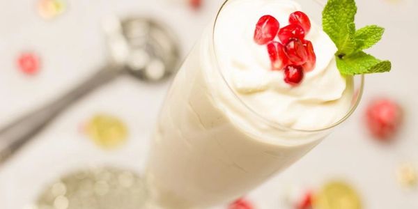 A tall glass of creamy white syllabub is dotted with pomegranate seeds and a sprig of mint.