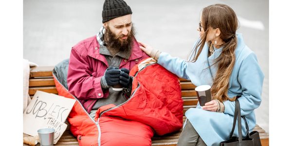 Woman comforting a homeless man on a bench.