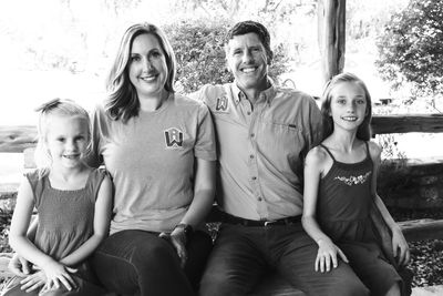 A happy family of four sitting together on a bench outdoors.