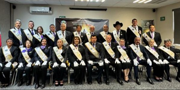 Group of formally dressed individuals wearing sashes and gloves in a conference room.