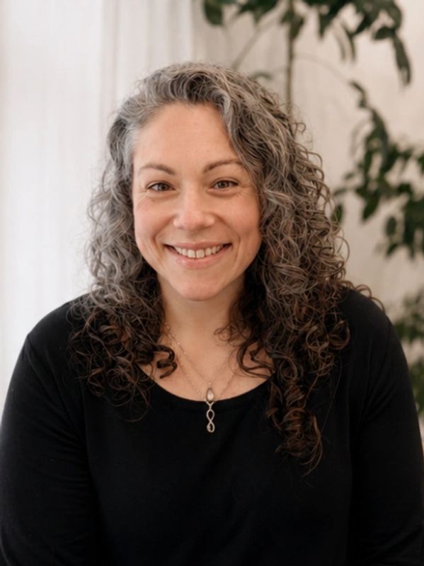 Smiling woman with curly gray hair wearing a black top and necklace.