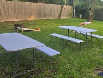 Outdoor picnic tables and a cornhole game set up on grass.