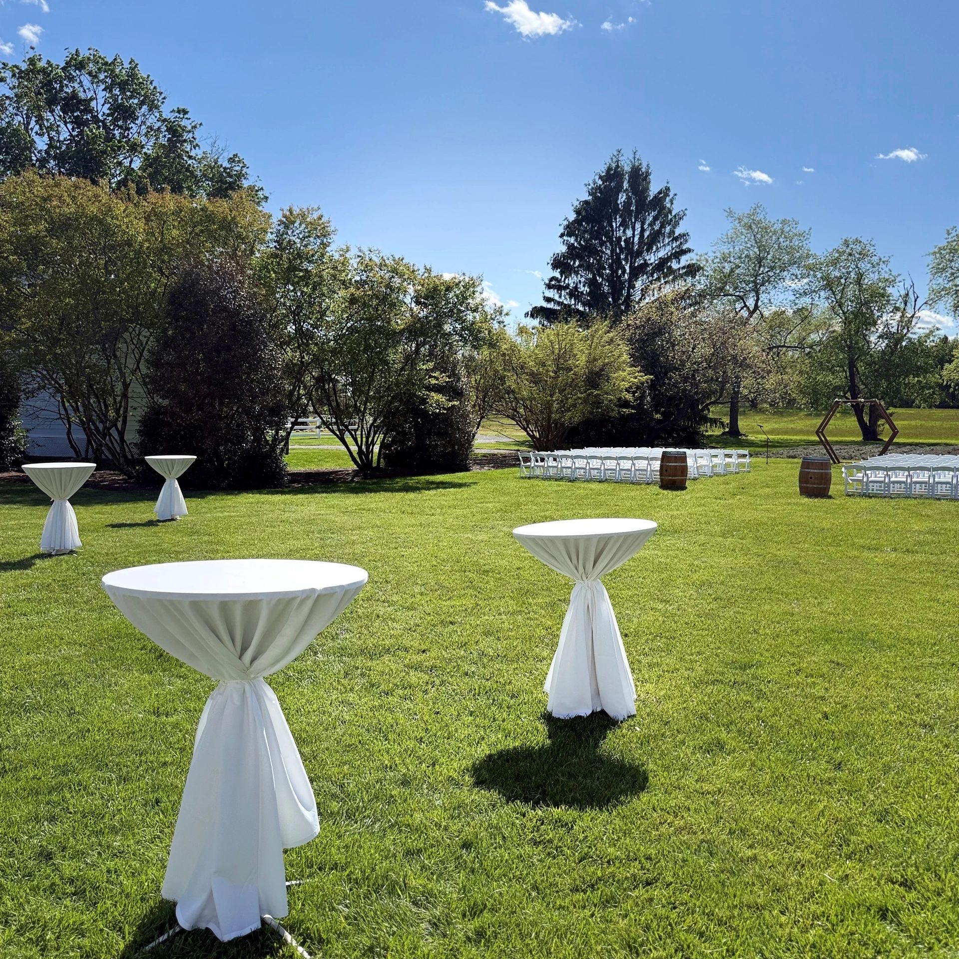 Outdoor event setup with white tables and chairs on a sunny day.