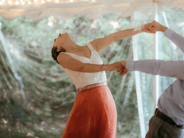 Woman in a white top and orange skirt dancing joyfully, holding hands with a partner.