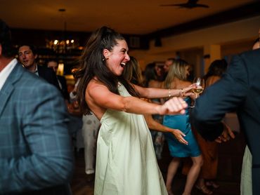 Woman joyfully dancing at a lively indoor party with a glass of wine.