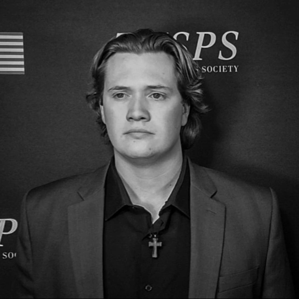 Young man in suit with cross necklace at a formal event.