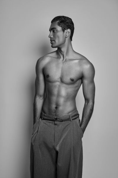 Black and white portrait of a shirtless man looking sideways with hands in pockets.