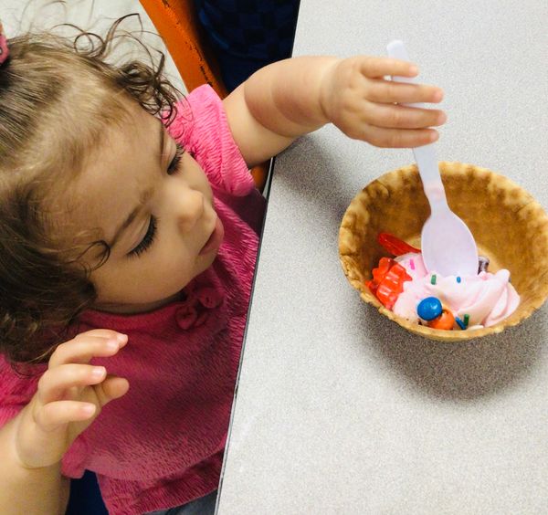 Toddler reaching for ice cream in a waffle bowl.