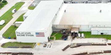Aerial view of Nucor Building Systems facility with parking and steel beams.