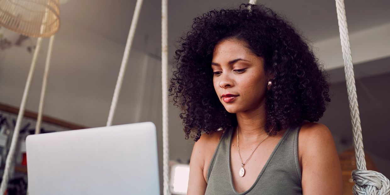 Mulher negra, jovem, veste camiseta verde, está usando o computador notebook.