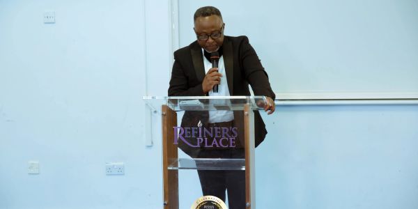 Man speaking at a podium with 'Refiner's Place' inscription.