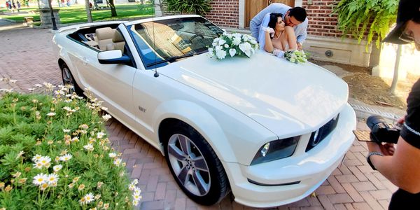 Newlywed couple posing on a white convertible car decorated with flowers.