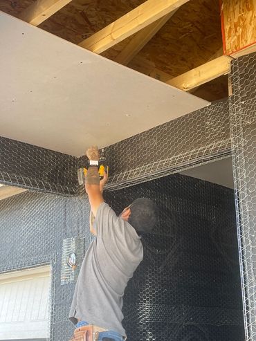A man using a drill to install a ceiling panel on a construction site.