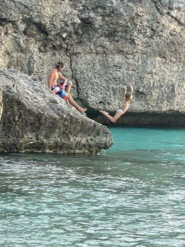 A person jumps into the water while another watches from a rocky ledge.