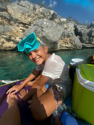 Smiling girl with snorkeling mask on a boat near rocky water cliffs.