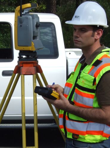 Surveyor using equipment beside a white pickup truck.