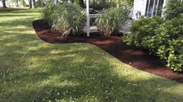 A neatly mulched garden bed curves alongside a green lawn near a house.