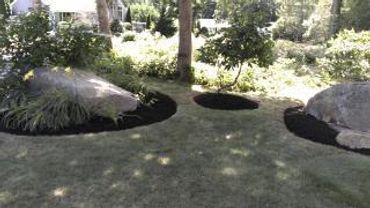 A garden with large rocks and freshly mulched circular beds on a grassy lawn.
