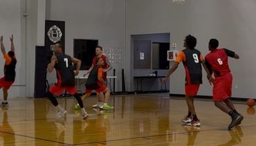 Basketball player in red shoots while defenders try to block inside a gym.