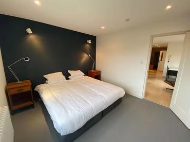 Minimalist bedroom with a large bed and bedside lamps against a dark accent wall.