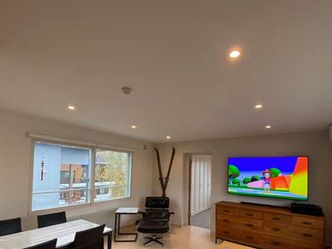 Modern living room with dining area, TV, and cozy seating under recessed lighting.