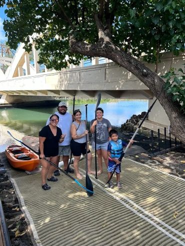 A family with paddles at Blue Planet Adventure Company in front of the Rainbow Bridge in Haleiwa
