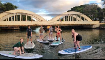 A group of Stand Up Paddleboarders in front of the Rainbow Bridge in Haleiwa on the Anahulu River