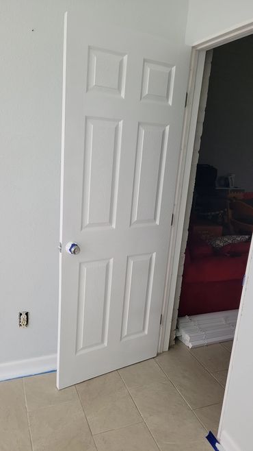 A white door partially open with a taped doorknob in a room under renovation.