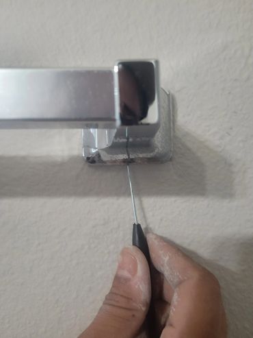 Hand using a tool to clean or scrape a metal towel bar mount on a wall.