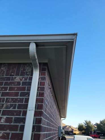 White gutter and downspout on a brick house against a clear blue sky.
