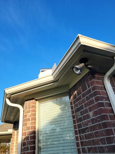 Corner of a brick house with a window and outdoor light under a blue sky.