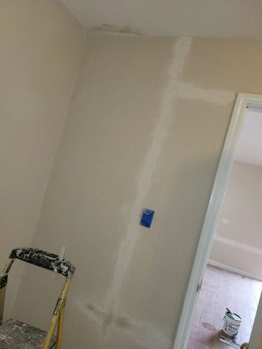 Wall undergoing patching and painting preparation with ladder and tools.