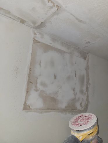 Wall patching and sanding in progress with a power sander visible.