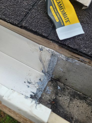 Gutter corner sealed with gray roofing sealant next to asphalt shingles.