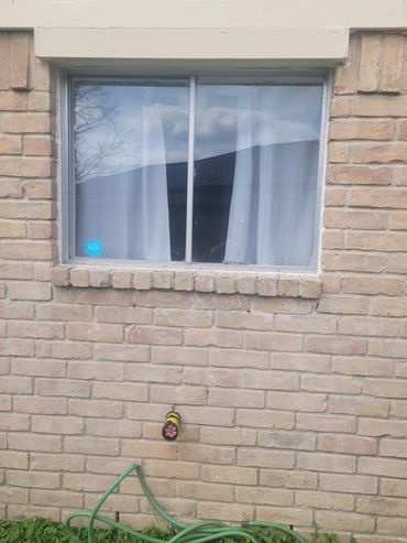 Brick wall with a window and a garden hose on green grass.