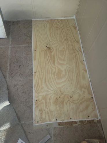A piece of plywood secured on a tiled floor next to a carpet.