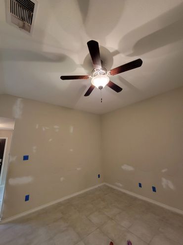 Empty room with ceiling fan, tiled floor, and taped wall patches.