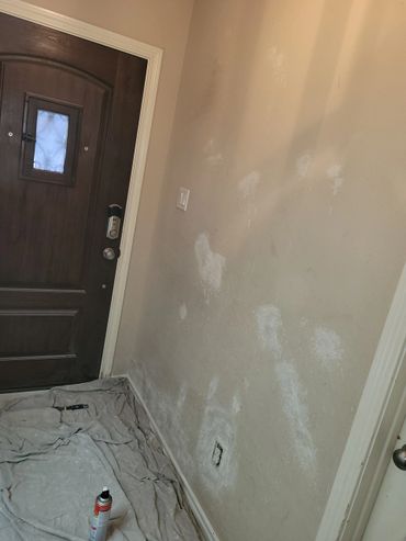 Patching and prepping wall near a dark wooden door for painting.