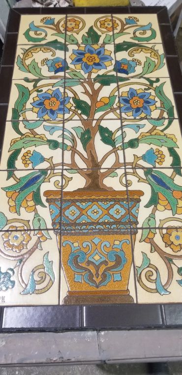Handcrafted ceramic tile artwork mural featuring a flowering tree and decorative planter inspired by California art tile traditions.