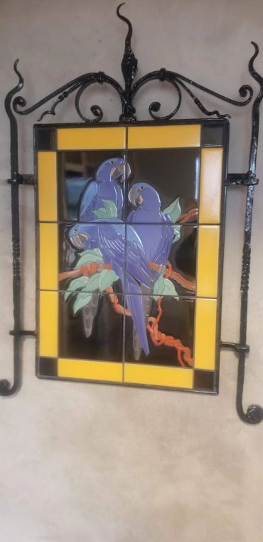 Handcrafted decorative tile mural featuring blue parrots and tropical foliage inspired by vintage Malibu tile art.