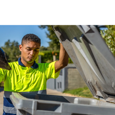 A valet trash worker collects trash in a trash can.